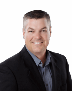 A smiling man in a collared gray shirt and black blazer