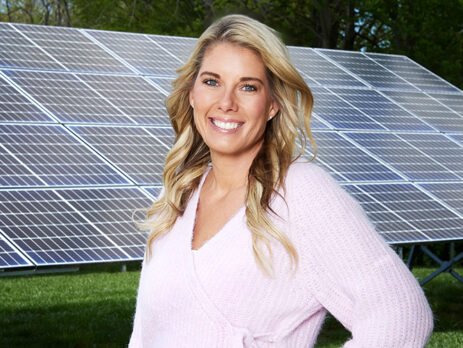A woman in a pink sweater standing in front of a ground-mounted solar array
