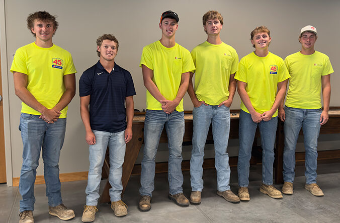 Six young male adults in jeans smile and stand in a row