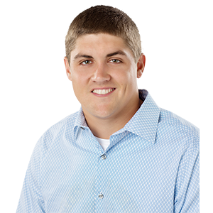 A smiling man with dark hair in a light blue collared shirt