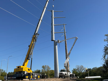 A yellow crane sets a metal electrical pole