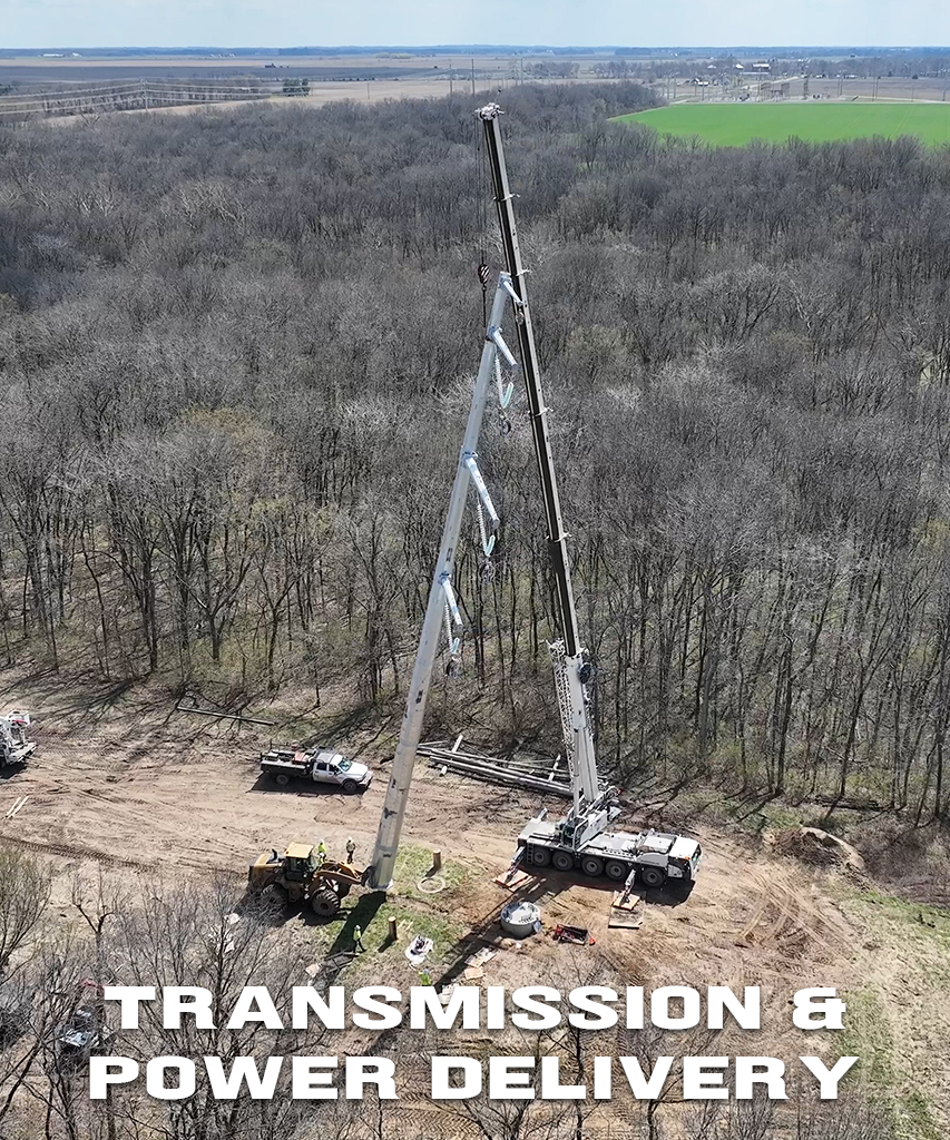 A large crane brings a tall utility pole erect